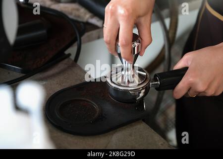 Eine Arbeiterin drückt geröstete Kaffeebohnen mit einem Stampfer, bevor sie in die Kaffeemaschine gegeben werden Stockfoto