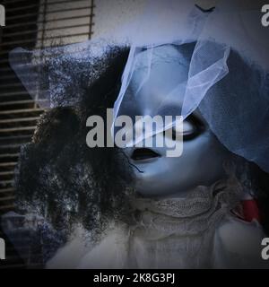 Horror Vintage Puppe mit weißen Augenhöhlen, die elegante Haube mit Schleier trägt. Eindringliche Kinderpuppe Gesicht. Halloween Hintergrund Stockfoto