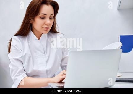 Ärztin in weißer medizinischer Uniform mit Laptop Stockfoto