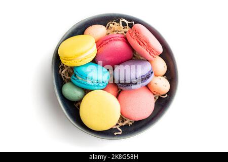 Bunte Makronen und Schokoladeneier in blauer Keramikschale isoliert auf weißem Hintergrund. Draufsicht, Nahaufnahme, Stillleben. Frühstück, Morgen, conce Stockfoto