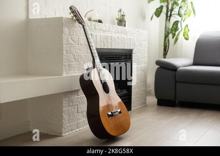 Minimalistisches Innenraumkonzept. Akustikgitarre auf grauem Textil-Sofa in geräumigen Zimmer im Loft-Stil Wohnung mit Holz strukturiert laminiert Stockfoto