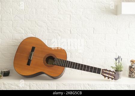 Minimalistisches Innenraumkonzept. Akustikgitarre auf grauem Textil-Sofa in geräumigen Zimmer im Loft-Stil Wohnung mit Holz strukturiert laminiert Stockfoto