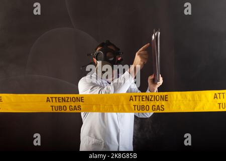 Ein Medizintechniker hält einen Dokumentenordner, der Notizen macht, chemische Schutzkleidung trägt und Antigas Mask leitet den Notfall im Chaos während Stockfoto