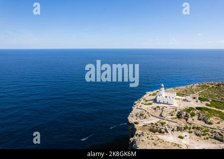 Von oben herrliche Fernsicht auf den Leuchtturm von Cape Cavalleria, der sich an sonnigen Tagen auf Menorca, Spanien, auf grünen Felsklippen vor dem ruhigen Meer befindet Stockfoto