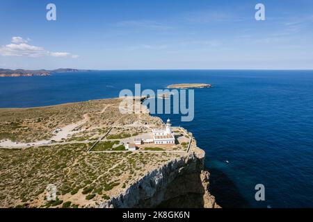 Von oben herrliche Fernsicht auf den Leuchtturm von Cape Cavalleria, der sich an sonnigen Tagen auf Menorca, Spanien, auf grünen Felsklippen vor dem ruhigen Meer befindet Stockfoto