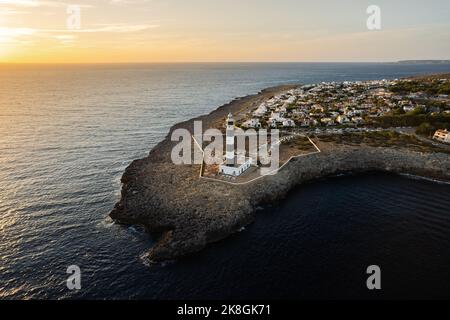 Von oben erstaunliche abgelegene Ansicht des Leuchtturms auf felsigen Klippen vor dem ruhigen Meer in der Nähe der Stadt mit weißen Häusern in Menorca, Spanien Stockfoto