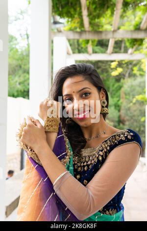 Junge ethnische indische Frau in stilvollem, traditionellem Sari und Schmuck, die im grünen Park mit Blick auf die Kamera steht Stockfoto