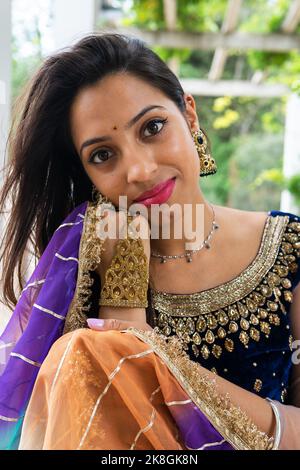 Junge ethnische indische Frau in stilvollem, traditionellem Sari und Schmuck, die im grünen Park mit Blick auf die Kamera steht Stockfoto