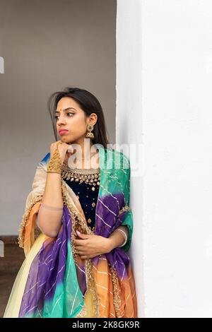 Nachdenkliche junge indische Frau in traditioneller Kleidung und Schal lächelnd und wegblickend im grünen Park Stockfoto