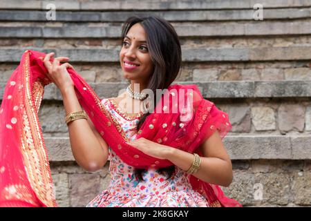 Fröhliche junge indische Hündin im traditionellen Sari-Outfit lächelnd und in der Nähe uralter Steinstufen wegblickend Stockfoto