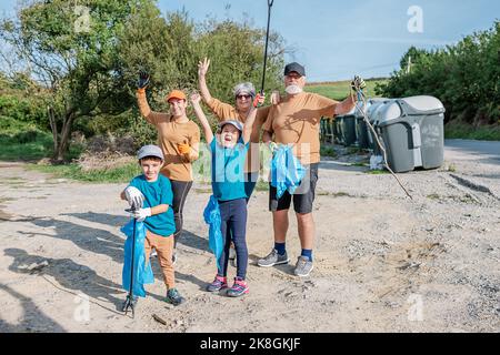 Eine Gruppe von Freiwilligen mit erhobenen Armen, während sie am sonnigen Tag Müll auf dem Land pflücken Stockfoto