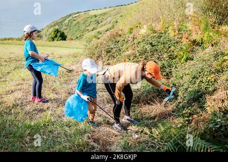 Aufräumarbeiten Freiwillige sammeln Müll in Mülltüten mit Stöcken auf Gras während der Umweltkampagne auf dem Land Stockfoto