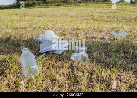 Gebrauchte Plastikflasche und gebrauchter Becher in der Nähe von zerknitterter Folie auf grasbewachsener Wiese Stockfoto