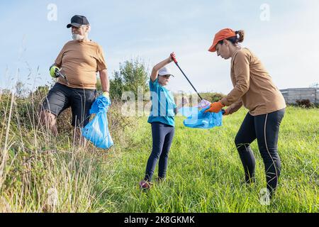 Aufräumarbeiten Freiwillige sammeln Müll in Mülltüten mit Stöcken auf Gras während der Umweltkampagne auf dem Land Stockfoto