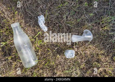 Draufsicht auf gebrauchte Plastikflasche und gebrauchten Becher in der Nähe von zerknitterter Folie auf grasbewachsener Wiese Stockfoto