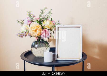 Leeres, leeres, leeres Modell eines weißen Fotorahmens mit Rosenstrauß und Kerze. Inneneinrichtung auf dem Tisch. Leerzeichen auf weißem Hintergrund Stockfoto