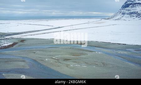 Von oben geradeaus asphaltierte Straße durch Feuchtgebiet in der Nähe verschneiten Berges an kalten Wintertag in der Landschaft von Island Stockfoto