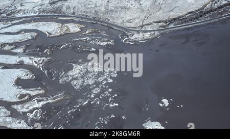 Von oben geradeaus asphaltierte Straße durch Feuchtgebiet in der Nähe verschneiten Berges an kalten Wintertag in der Landschaft von Island Stockfoto