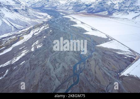 Von oben geradeaus asphaltierte Straße durch Feuchtgebiet in der Nähe verschneiten Berges an kalten Wintertag in der Landschaft von Island Stockfoto