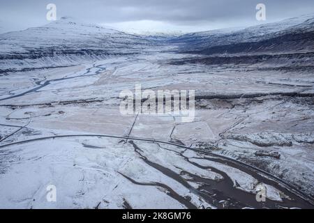 Von oben geradeaus asphaltierte Straße durch Feuchtgebiet in der Nähe verschneiten Berges an kalten Wintertag in der Landschaft von Island Stockfoto