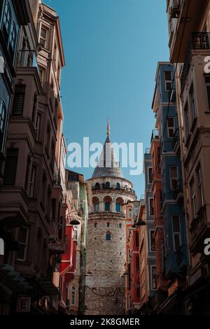 Von unten der berühmte Galata-Turm, der sich hinter Häusern am Ende einer schmalen Straße befindet, an wolkenlosen Tagen in Istanbul, Türkei Stockfoto