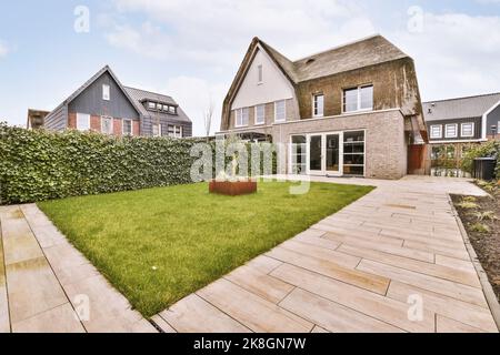 Terrasse des Wohngebäudes mit Tisch auf gepflasterter Terrasse mit kleinem Rasen in der Landschaft am Sommertag platziert Stockfoto