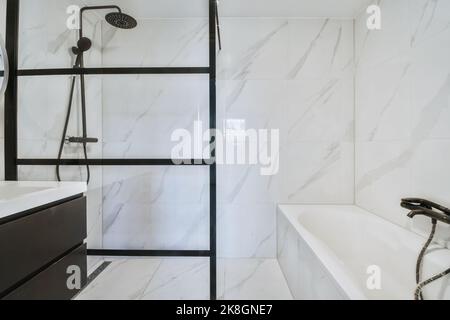 Stilvolles Badezimmer-Interieur mit Marmorfliesen und Fenstern ausgestattet mit Dusche und luxuriöser Badewanne in modernem Apartment Stockfoto