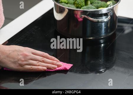 Frau, die Induktionsfläche reinigt. Die weibliche Hand wischt das Kochfeld des Induktionskochers ab. Stockfoto