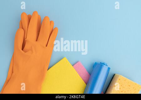 Schwamm zum Spülen, farbige Mikrofasertücher und Gummihandschuhe, Müllbeutel mit Rahmen auf blauem Hintergrund ausgelegt, Reinigungswerkzeug-Konzept mit Stockfoto