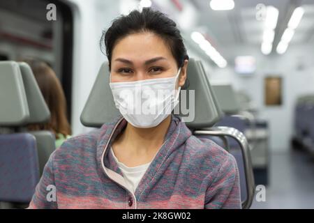 Frau in Maske, die im Stadtzug unterwegs ist Stockfoto