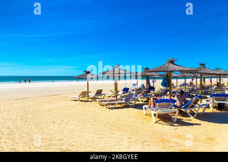 Strohsonnenschirme und Menschen auf Liegestühlen am Playa de la Barrosa, Cadaz, Spanien Stockfoto