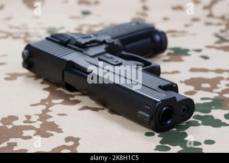 Moderne Handfeuerwaffe auf getarnter Uniform-Hintergrund Stockfoto