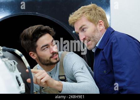 Zwei Arbeiter, die Isoliermaterial auf einen Industriekessel auftragen Stockfoto