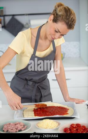 Nahaufnahme der Zugabe von Tomatensauce auf Pizzabasis Stockfoto