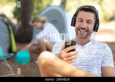 Junger Mann, der vor dem Zelt sitzt und Musik hört Stockfoto