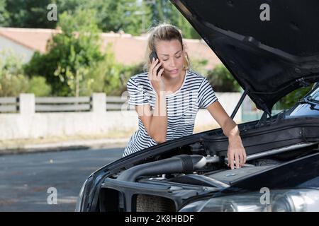 Gestresste Frau, die in der Nähe eines kaputten Autos ein Handy für Hilfe benutzte Stockfoto