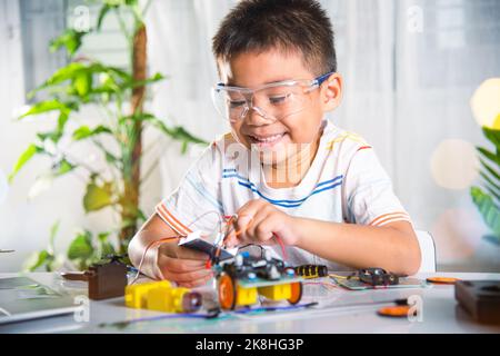 Kleines Kind aus der Ferne lernen online mit Auto-Spielzeug, bevor Code gesendet, asiatische Kind Junge stecken Energie-und Signalkabel an Sensor-Chip mit Arduino Roboterauto Stockfoto