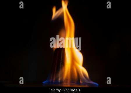 Flammen im Dunkeln. Zunge des Feuers eins. Flammhemmung durch Alkohol. Gelbes Leuchten auf schwarzem Hintergrund. Stockfoto