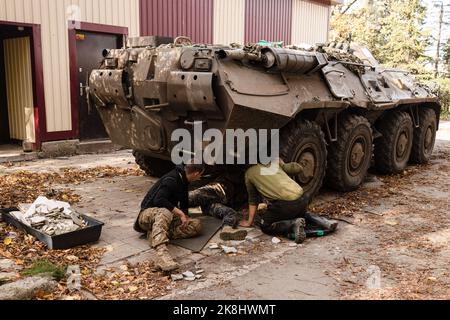 Ukrainische Soldaten wechseln die Reifen auf einem APC, einem gepanzerten persönlichen Träger der ukrainischen Armee in der Nähe eines beschädigten Gebäudes nach einem russischen Beschuss in der Stadt Bakhmut. Bakhmut ist eine der am schlimmsten beschossen Städte an den Fronten des Donbass-Krieges, seit Russland am 24. Februar 2022 seine umfassende Invasion in der Ukraine startete. Stockfoto