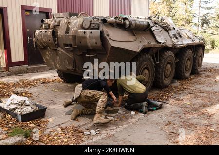 Ukrainische Soldaten wechseln die Reifen auf einem APC, einem gepanzerten persönlichen Träger der ukrainischen Armee in der Nähe eines beschädigten Gebäudes nach einem russischen Beschuss in der Stadt Bakhmut. Bakhmut ist eine der am schlimmsten beschossen Städte an den Fronten des Donbass-Krieges, seit Russland am 24. Februar 2022 seine umfassende Invasion in der Ukraine startete. Stockfoto