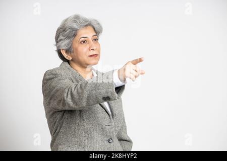 Reife ältere indische Geschäftsfrau Führer zeigen Finger in der Ferne isoliert auf weißem Hintergrund, Asian mittleren Alters Geschäftsfrau,60s grauhaarige Dame Stockfoto