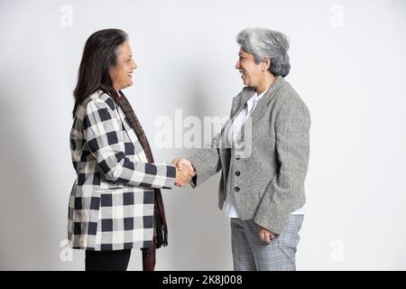 Zwei ältere indische Geschäftsfrau in einem Anzug Hand schütteln isoliert auf weißem Hintergrund. Lächelnd erfolgreiche asiatische 60s grauhaarige Dame Executive oder b Stockfoto