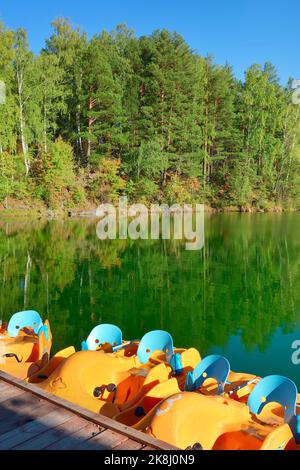 Aya-See im Altai-Gebirge. Wasservergnügungsboote am Pier zwischen den Pinien am felsigen Ufer. Altai, Sibirien, Russland, 2022 Stockfoto