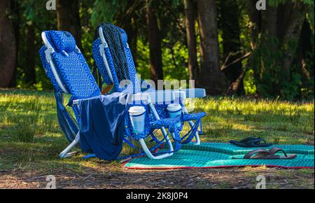 Zwei leere Klappstühle auf dem grünen Gras an einem sonnigen Tag. Zwei Stühle für ein Picknick im Sommerpark. Niemand, Reisefoto. Stockfoto