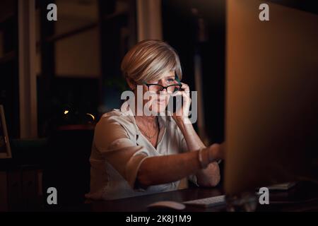 Arbeiten Sie hart, und die Belohnungen werden folgen. Eine attraktive reife Geschäftsfrau, die am Computer arbeitet und spät in der Nacht im Büro telefoniert. Stockfoto