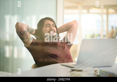 Hes ein solcher Profi in seinem Job. Ein junger Geschäftsmann, der eine Pause an seinem Schreibtisch nimmt. Stockfoto