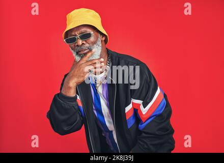 Hes ist so ein Charmeur. Studioaufnahme eines älteren Mannes in Retro-Kleidung, während er vor einem roten Hintergrund posiert. Stockfoto