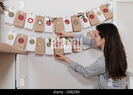 Mutter eröffnet Weihnachten Adventskalender Aufgaben und Geschenke. Frau begeistert von der festlichen Überraschung in der Basteltasche zu Hause. Familienfeier und Stockfoto