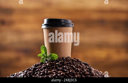 Jeder Schluck ist so beruhigend. Nahaufnahme eines Minzblatts und einer Papiertasse auf einem Stapel Kaffeebohnen. Stockfoto