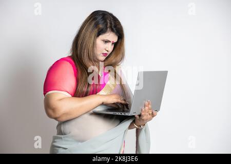 Porträt einer geschäftigen städtischen inderin mit Sari, die auf einem Laptop auf weißem Hintergrund arbeitet. Stockfoto